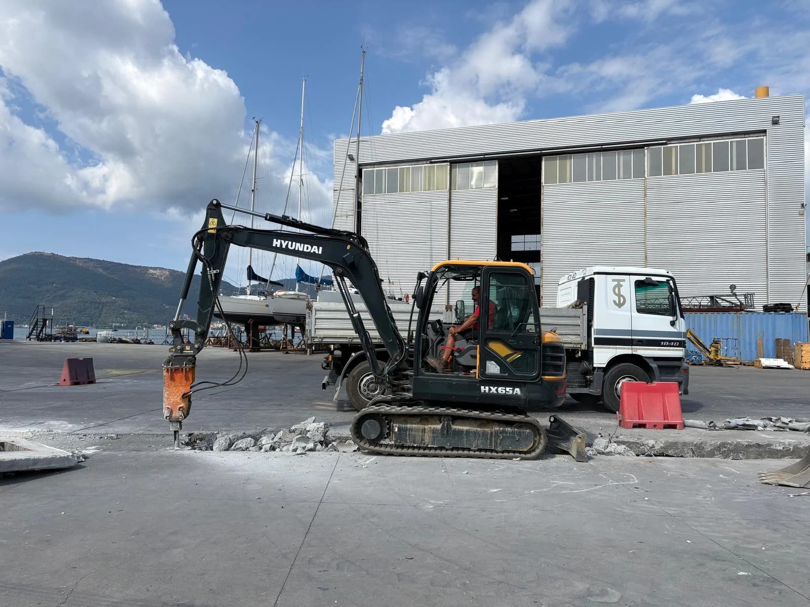 Escavatore con martello demolitore e camion a fianco del tratto di pavimentazione demolito