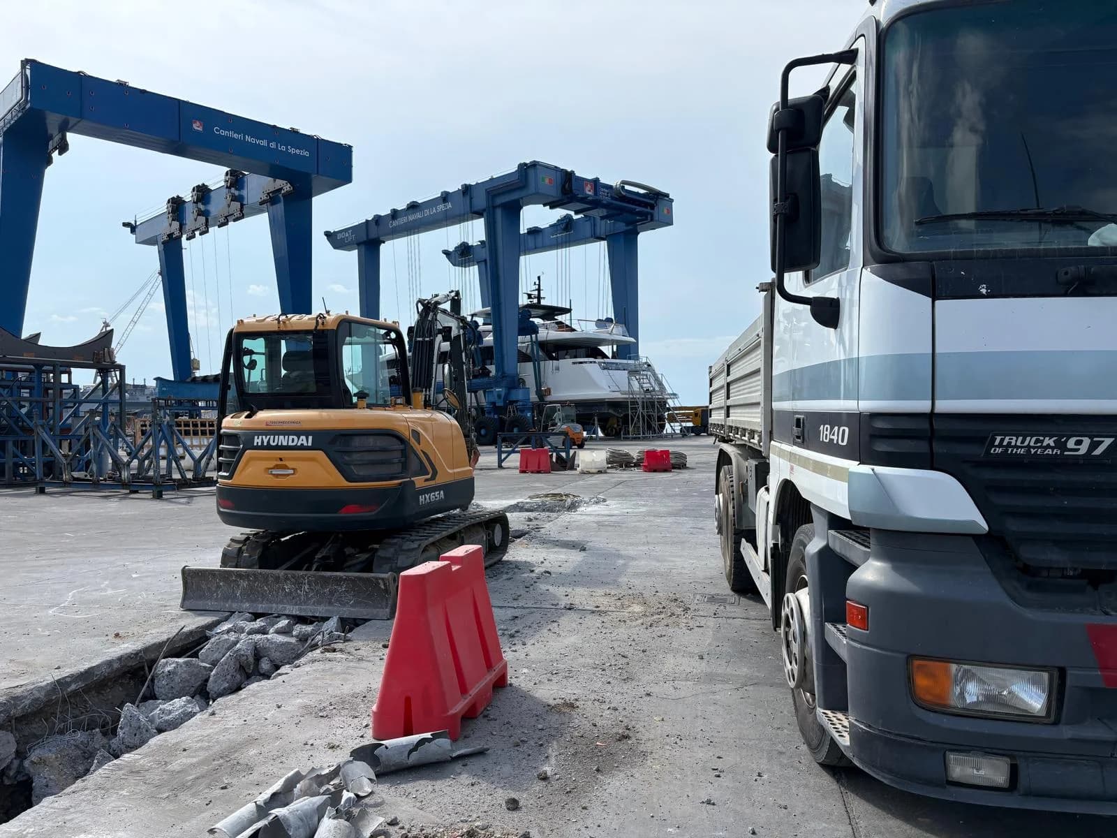 Tratto di pavimentazione demolito con detriti, escavatore e camion nel cantiere navale
